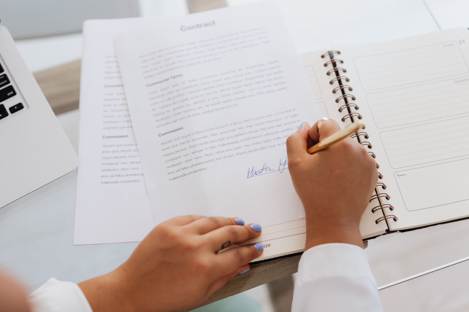 Hands signing a legal document at a desk beside a stack of paperwork